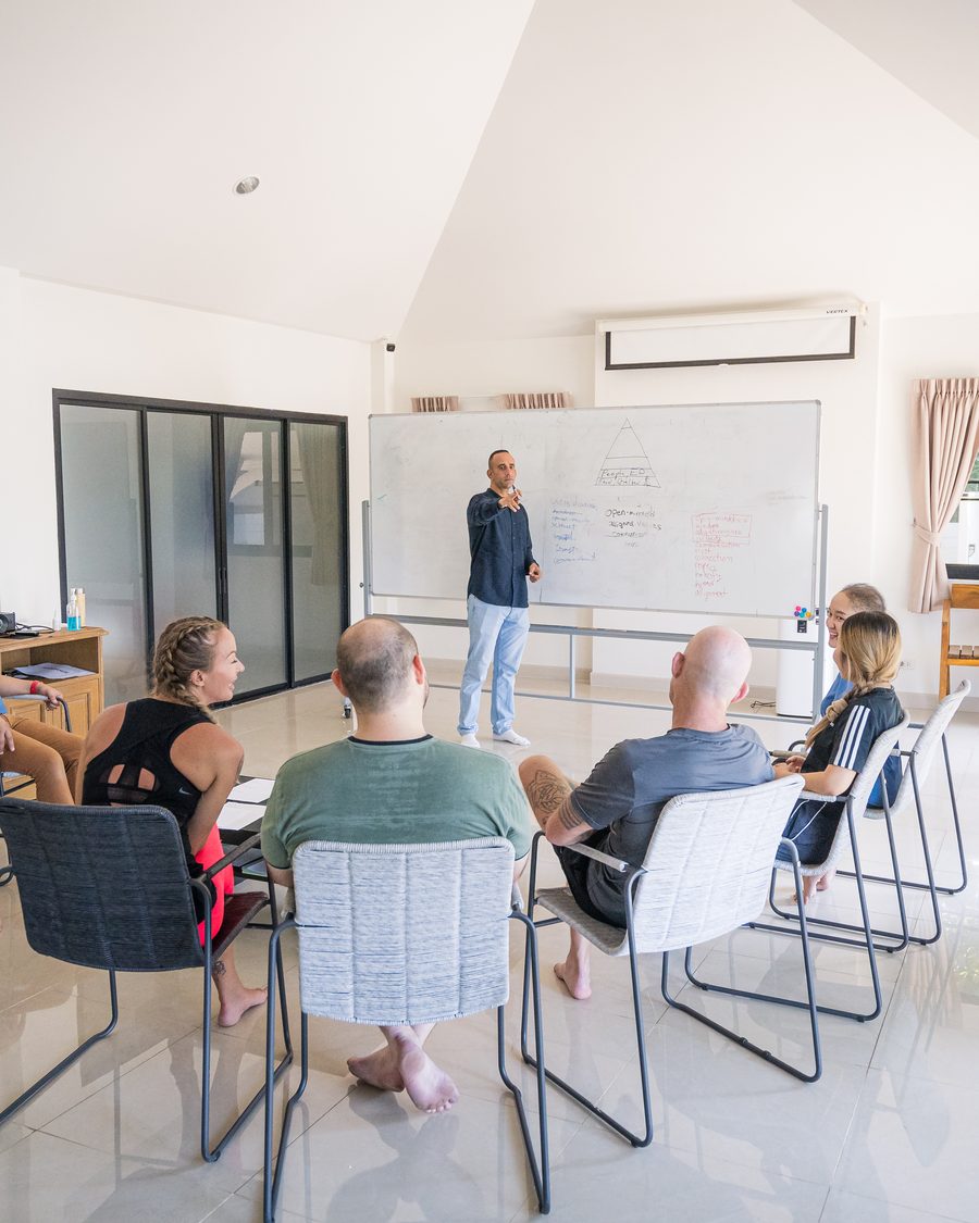 A clinician standing at a whiteboard, talking to a group seated in a circle of chairs