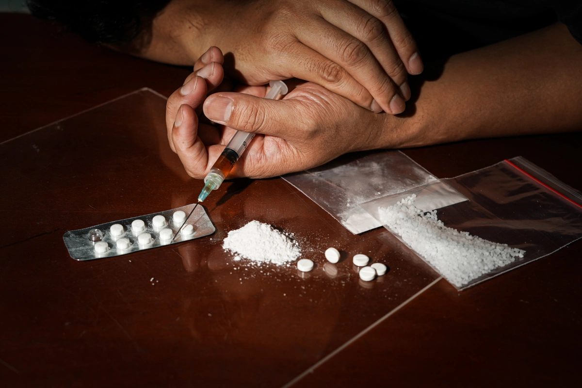 Close-up of hands preparing drugs with a syringe, pills and powder on a table