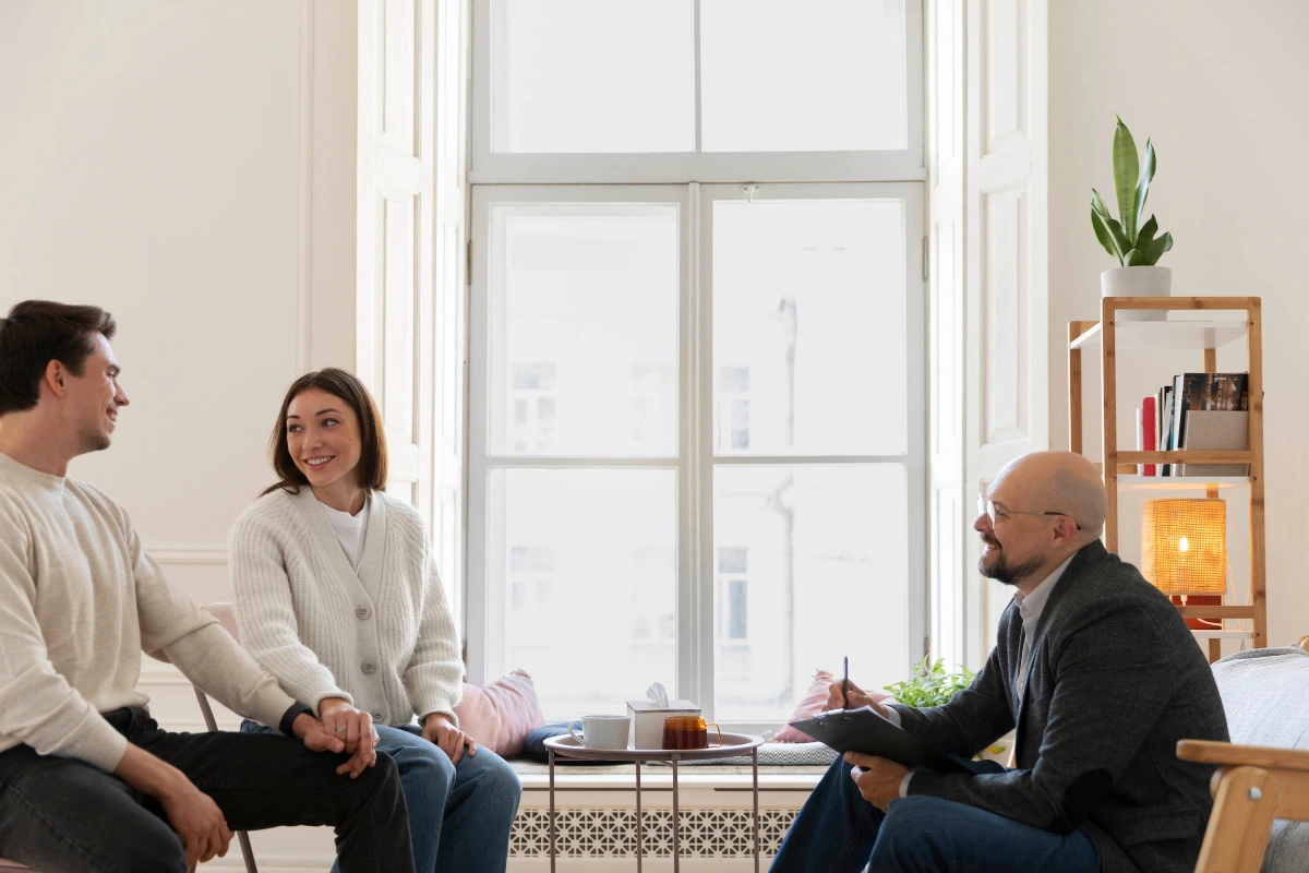 Two people in a therapy session with a psychologist in a bright room