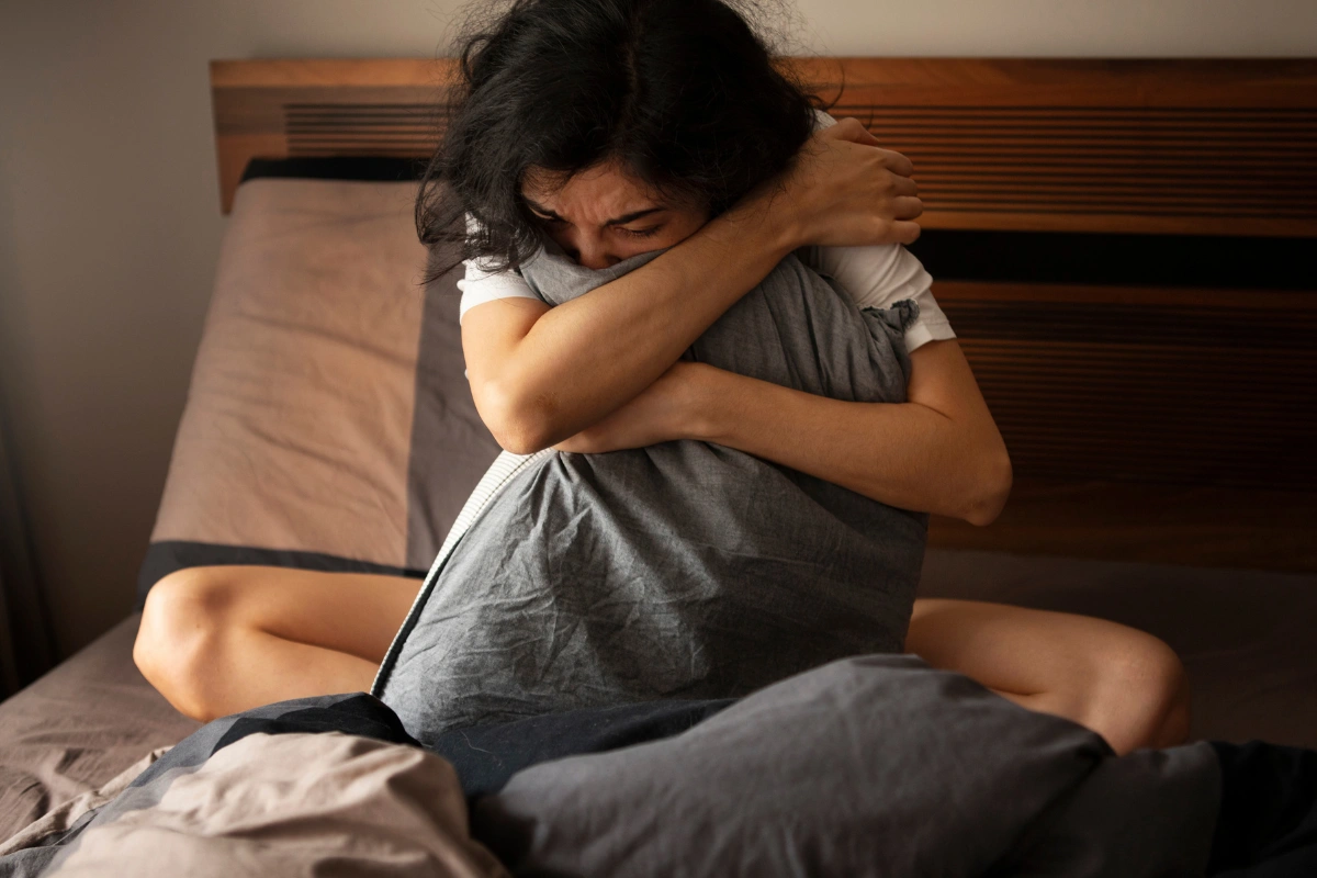 Distressed woman hugging a pillow on a bed, showing anxiety and depression