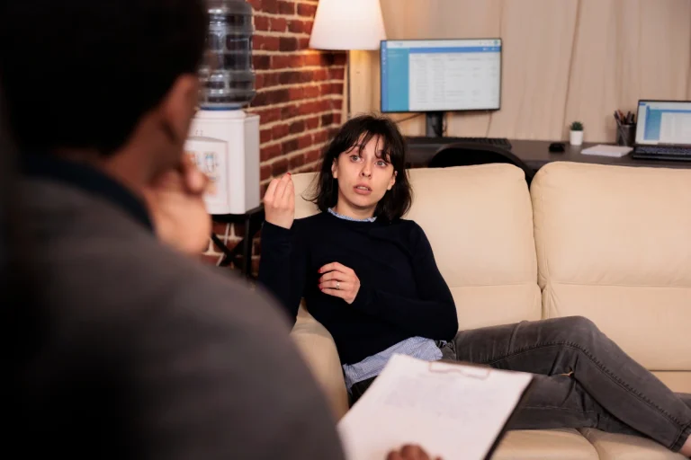 Woman experiencing symptoms of severe anxiety disorder sitting on a sofa in a dark room.