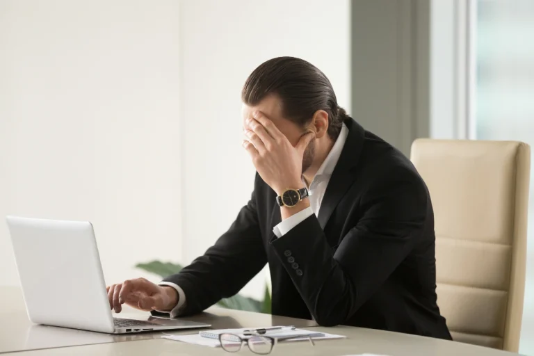 Stressed executive suffering from severe burnout sitting at a desk with a laptop, highlighting the need for executive burnout treatment in Thailand.