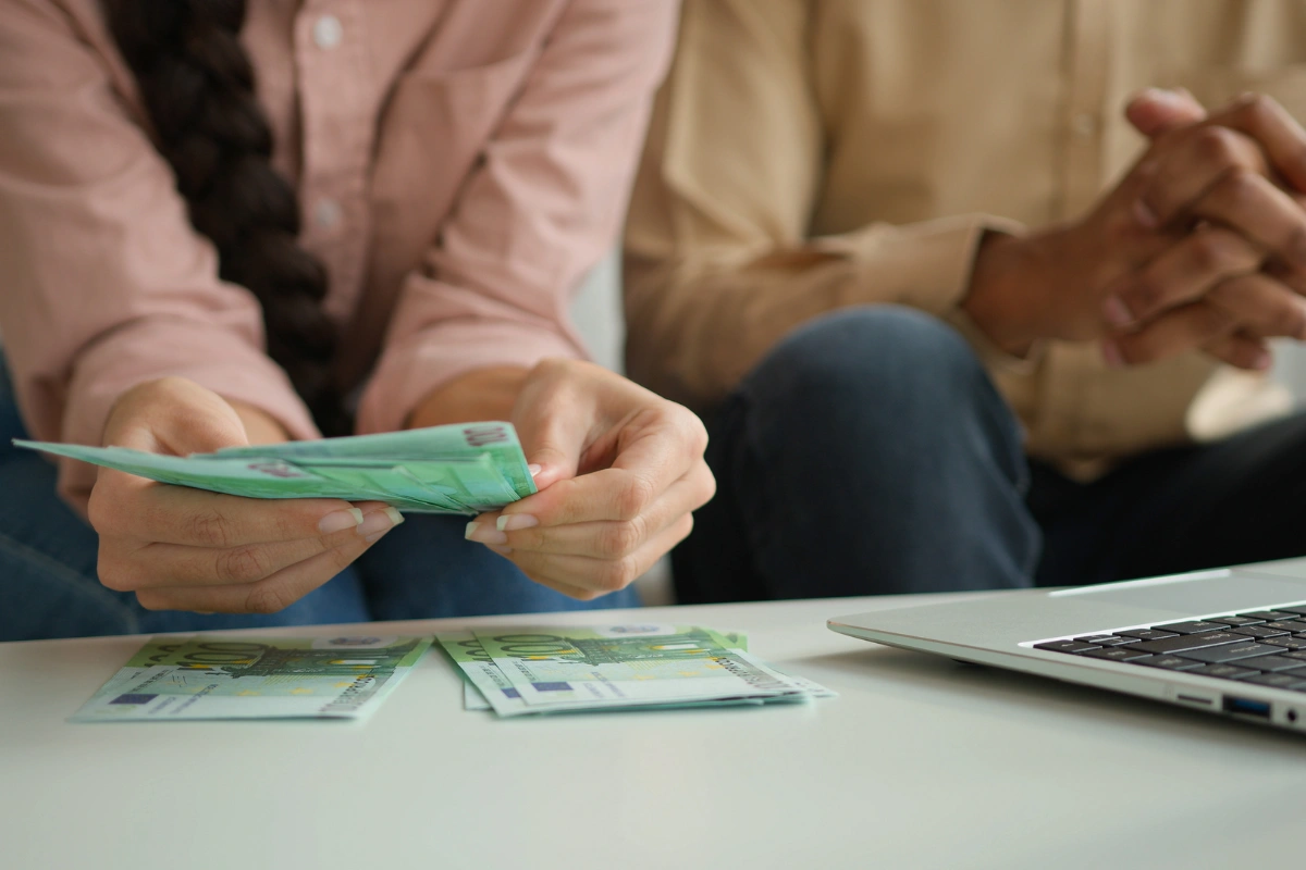 Couple managing cash expenses next to a laptop, illustrating the financial impact of severe gambling addiction.