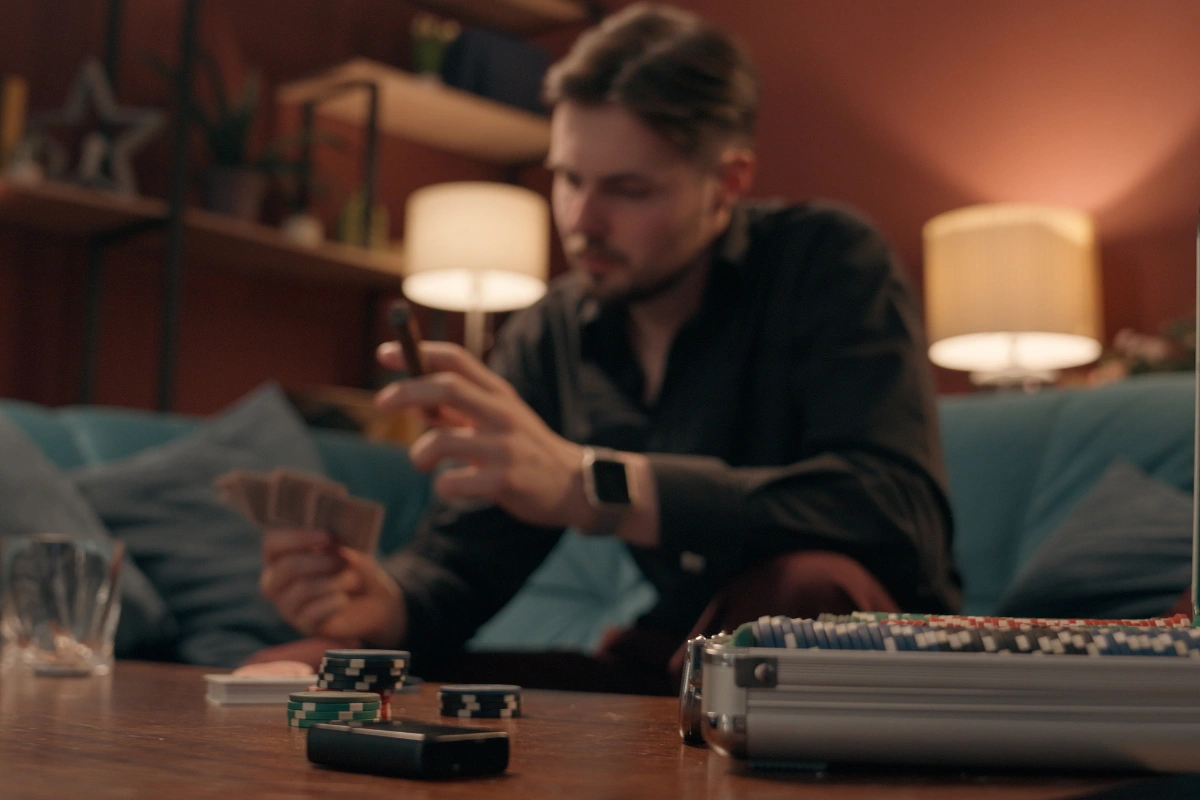 Man sitting at home with playing cards and a smartphone, showing the behavioral cycle behind online gambling addiction.