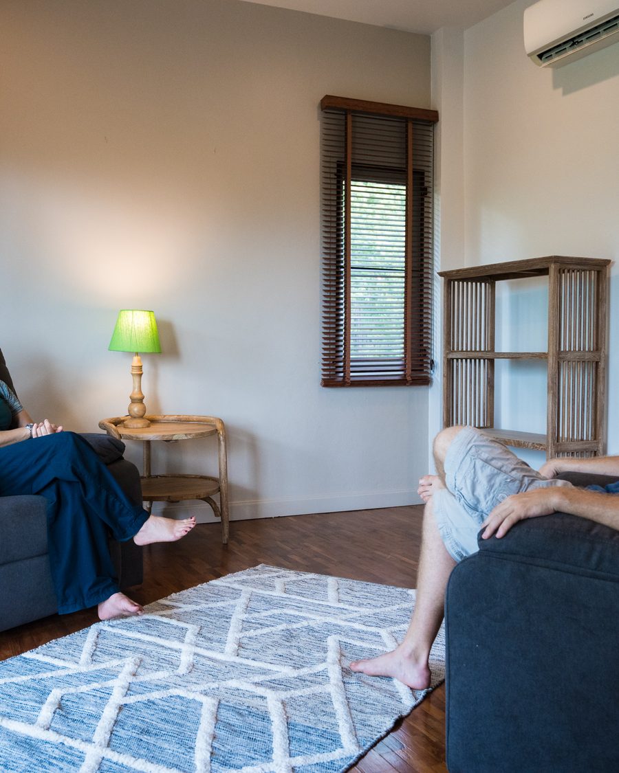 A one-to-one therapy room with two armchairs facing one another across a patterned rug, a lamp lit on the side table between them