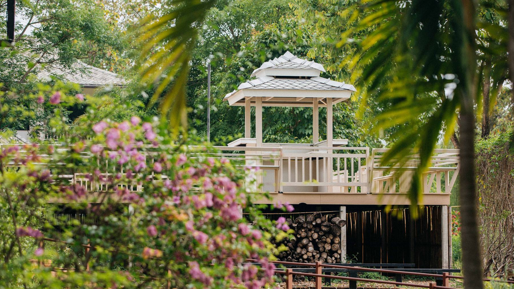 A raised sala pavilion in the grounds, seen through pink blossom and palm fronds