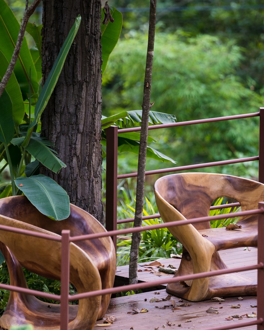 Two carved wooden chairs on the deck, looking out into the trees