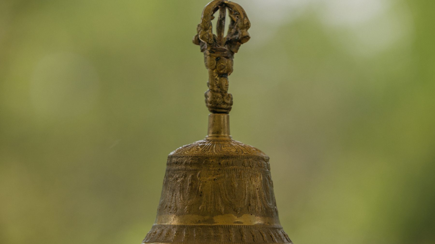 A brass ritual bell standing against the green of the gardens