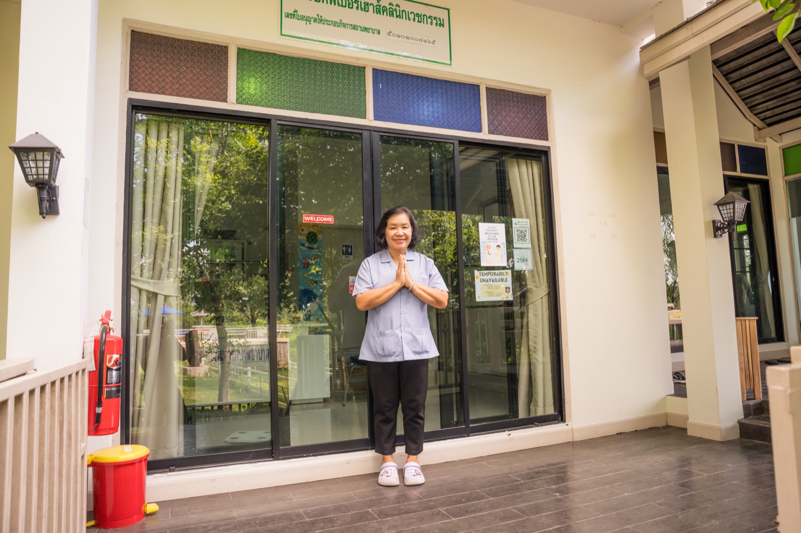 A nurse greeting a new arrival with a wai outside the glass doors of the on-site clinic